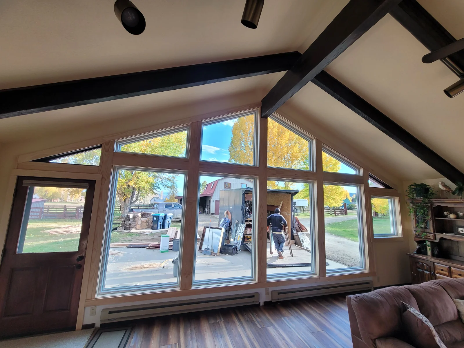 Large gable-shaped window wall with natural wood frame, silver-toned panes, and exposed dark wood ceiling beams