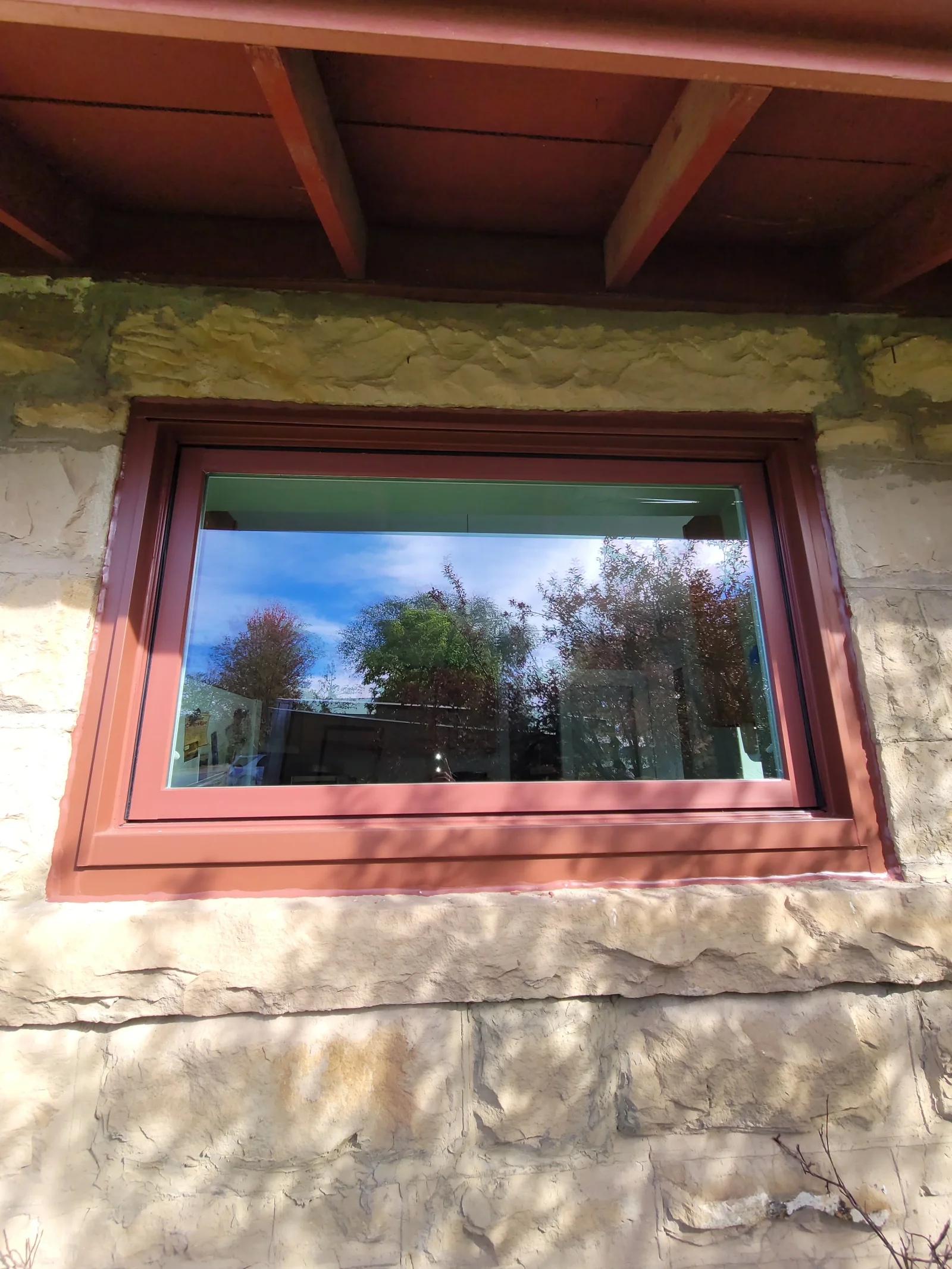 Reddish-brown window frame set into rough-cut stone wall beneath a wood soffit
